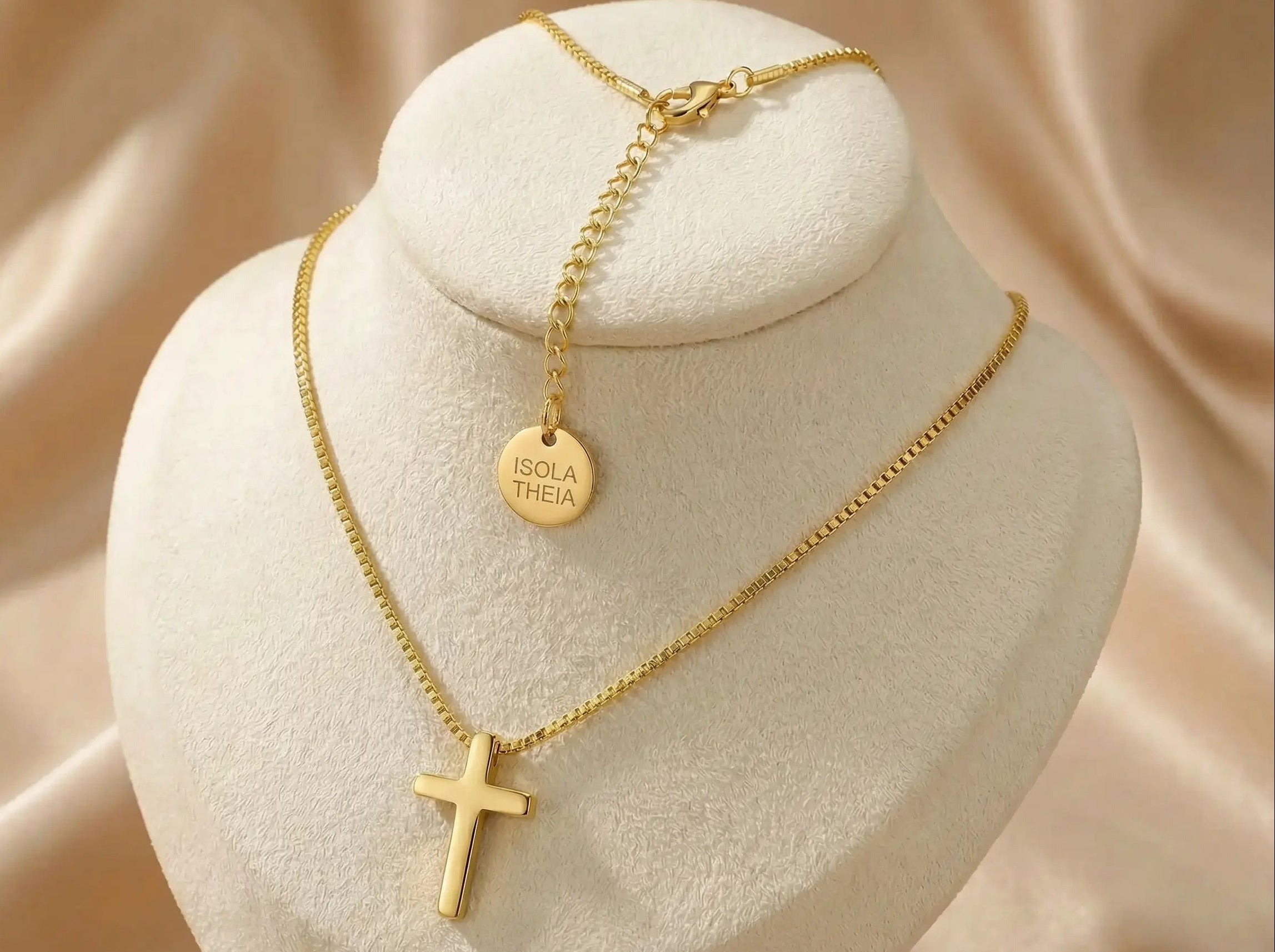 Gold necklace with a cross pendant on a white stand against a beige fabric background